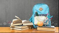 Back to school concept with school books, textbooks, backpack and stationery supplies on classroom desk with teacher's black cha
